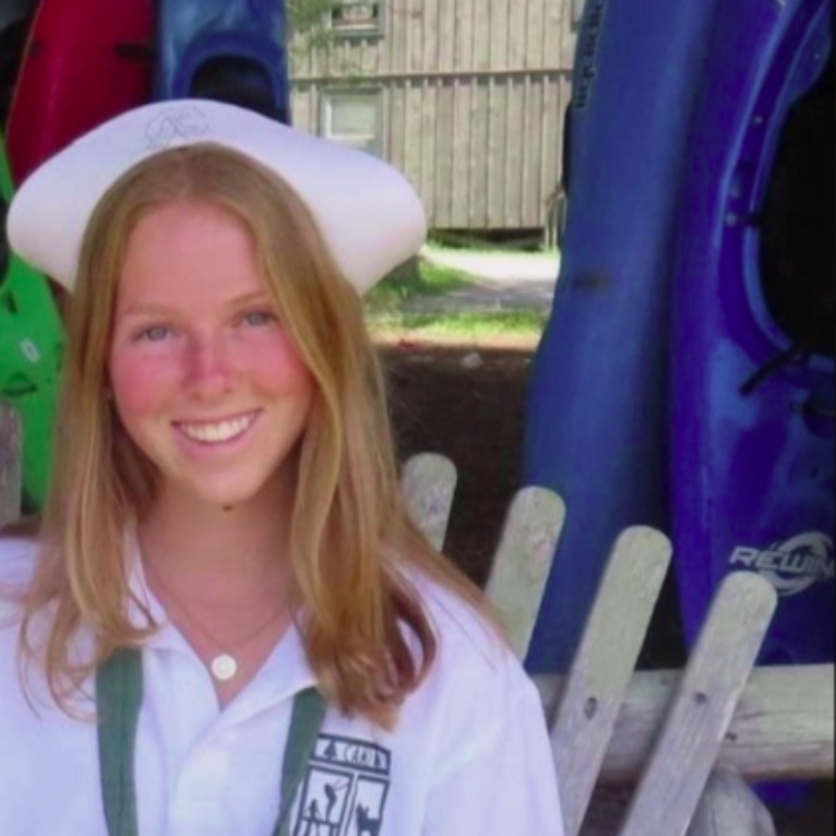 A smiling person wearing glasses and a 