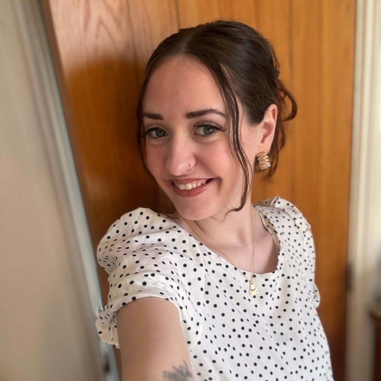 A person wearing a navy tank top and floral cardigan smiles while standing on a balcony overlooking a city and coastline.