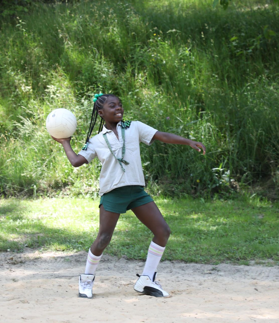 Four people splashing and smiling under a waterfall in bright swimwear.