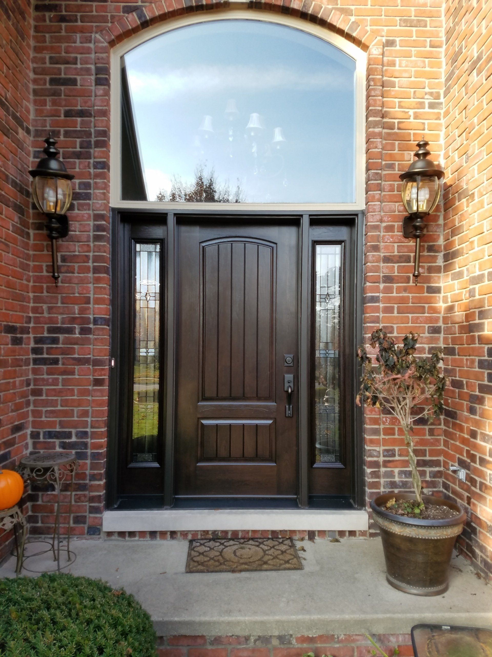 The front door of a brick house with a large window and a brown door.