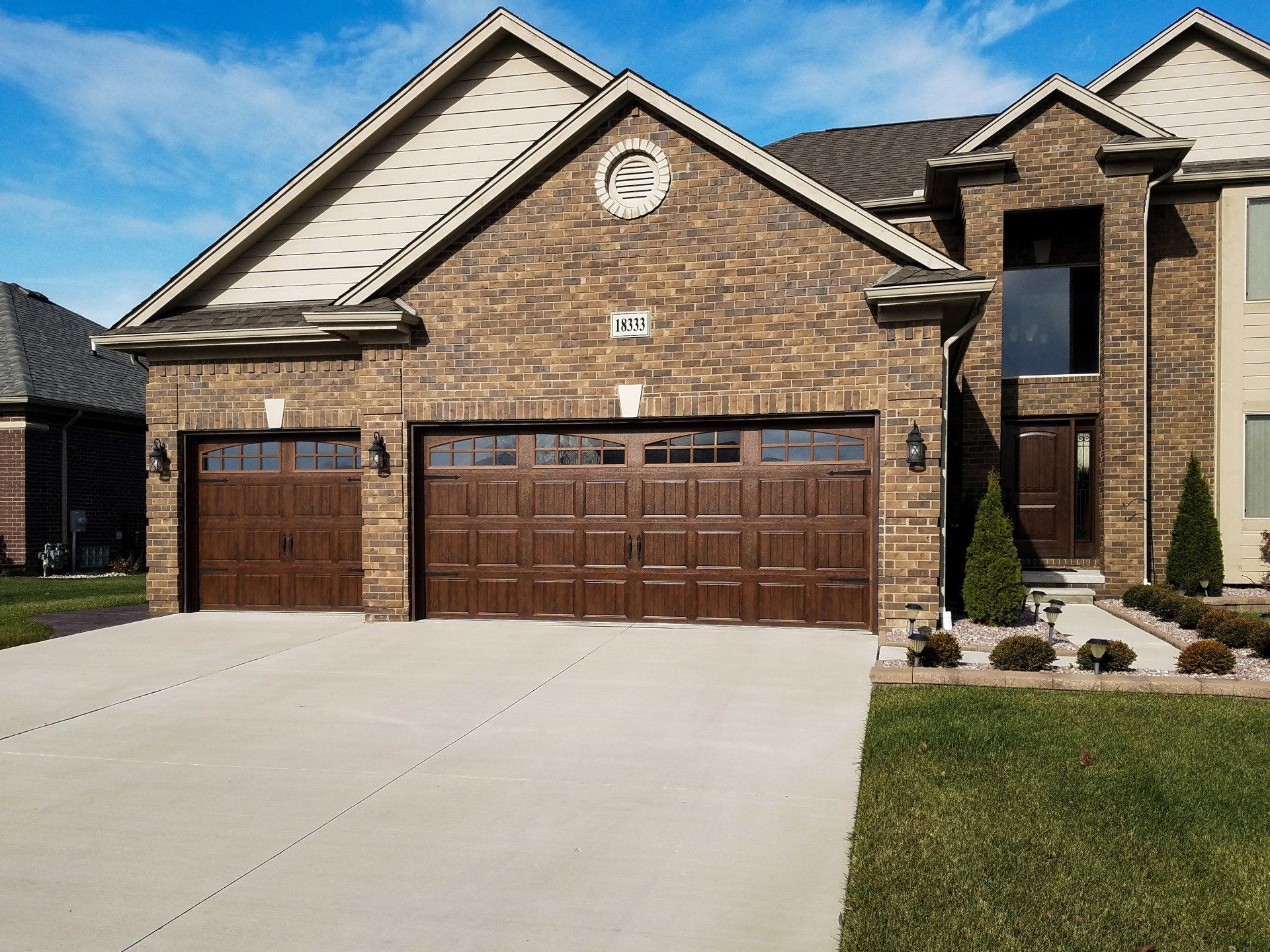 A large brick house with two garage doors and a concrete driveway.