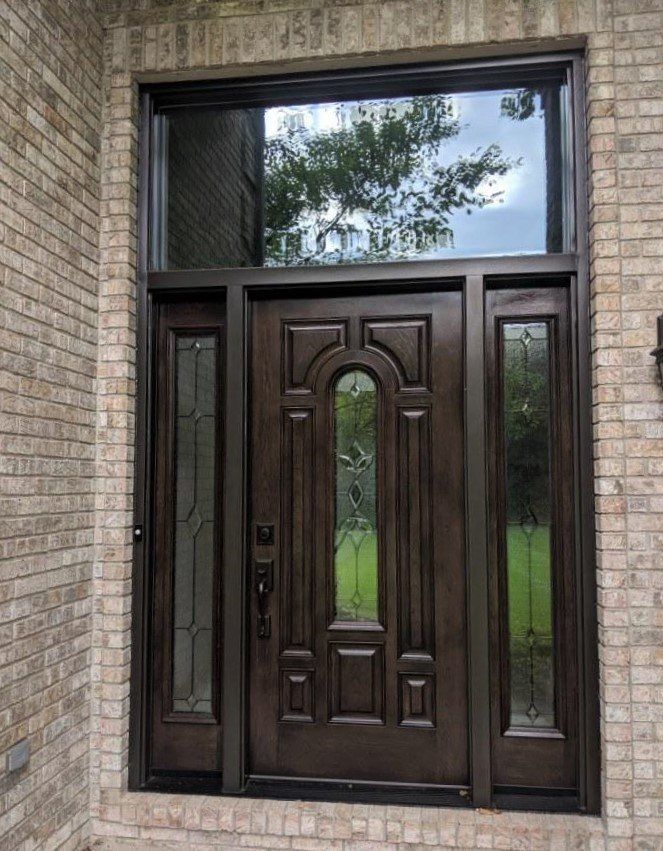 A large wooden door with a stained glass window is on a brick building.