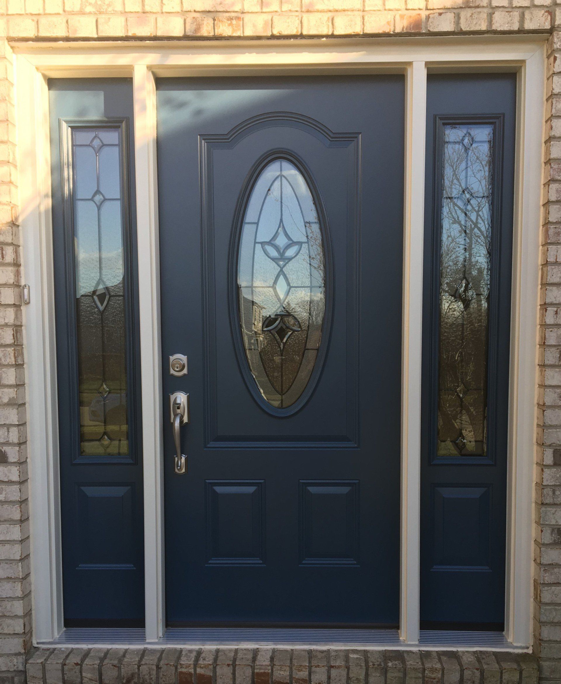 A black front door with a stained glass window is on a brick building.