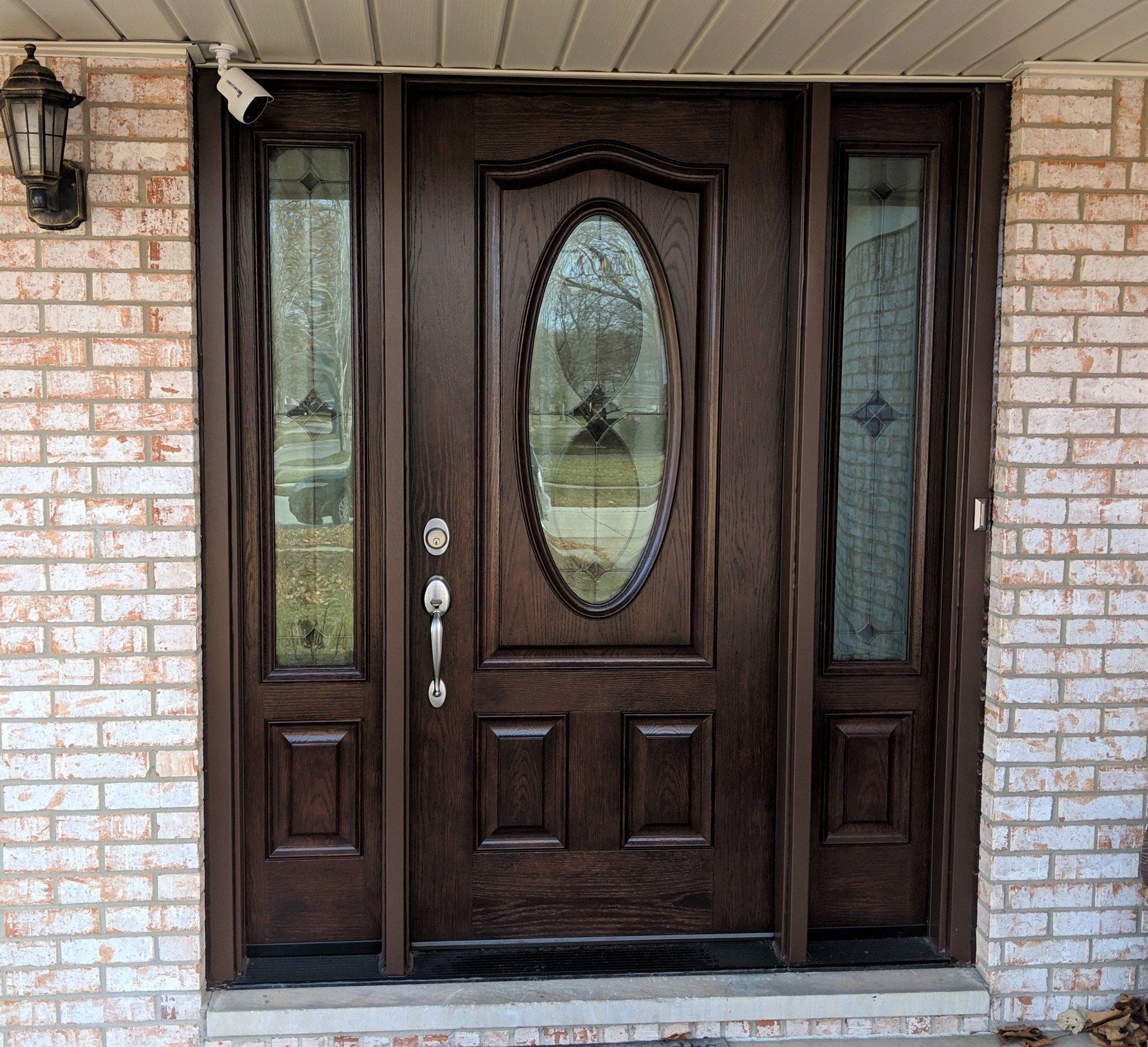 The front door of a brick house has a large oval window