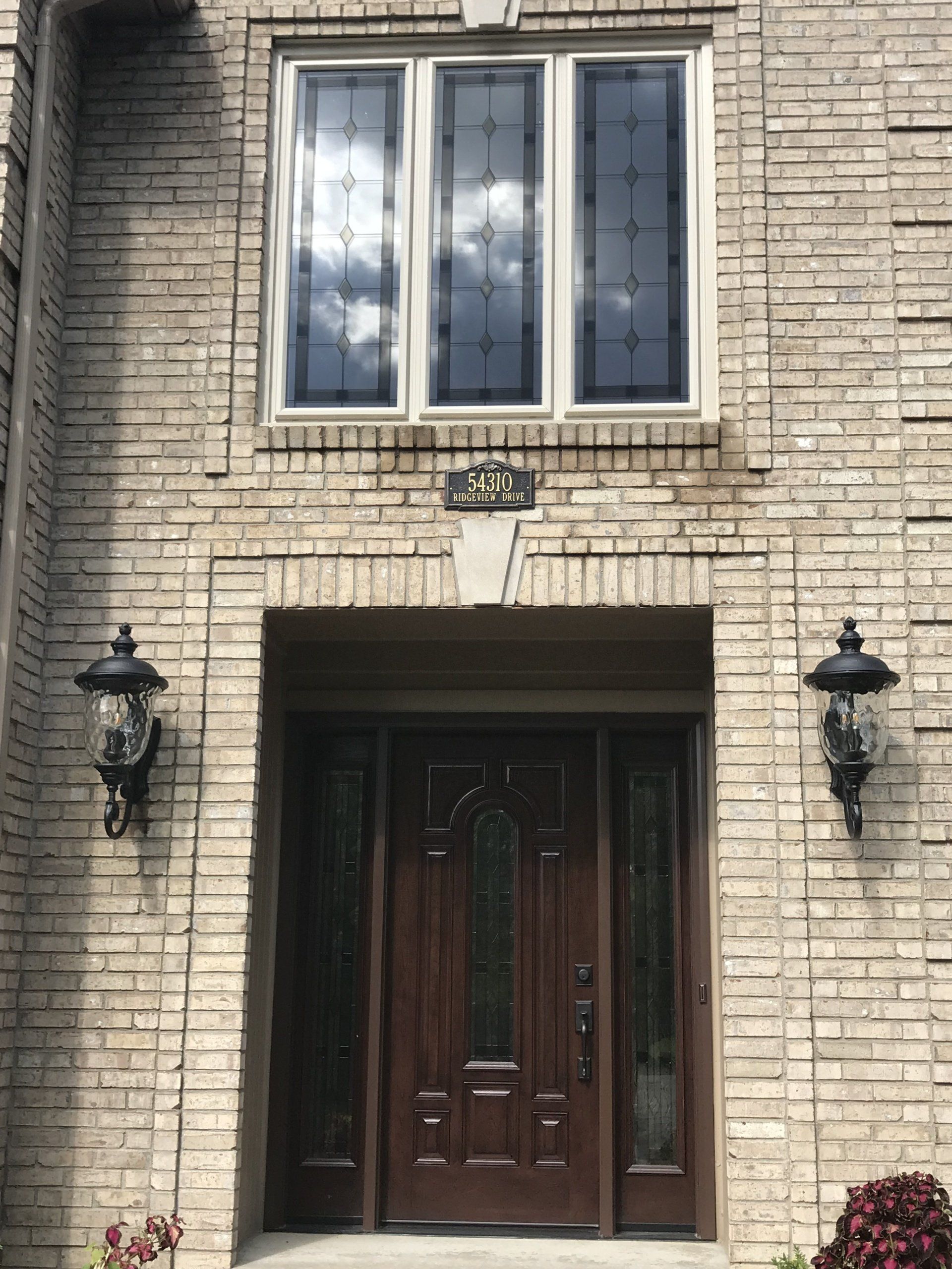 The front door of a brick house with a wooden door and three windows.
