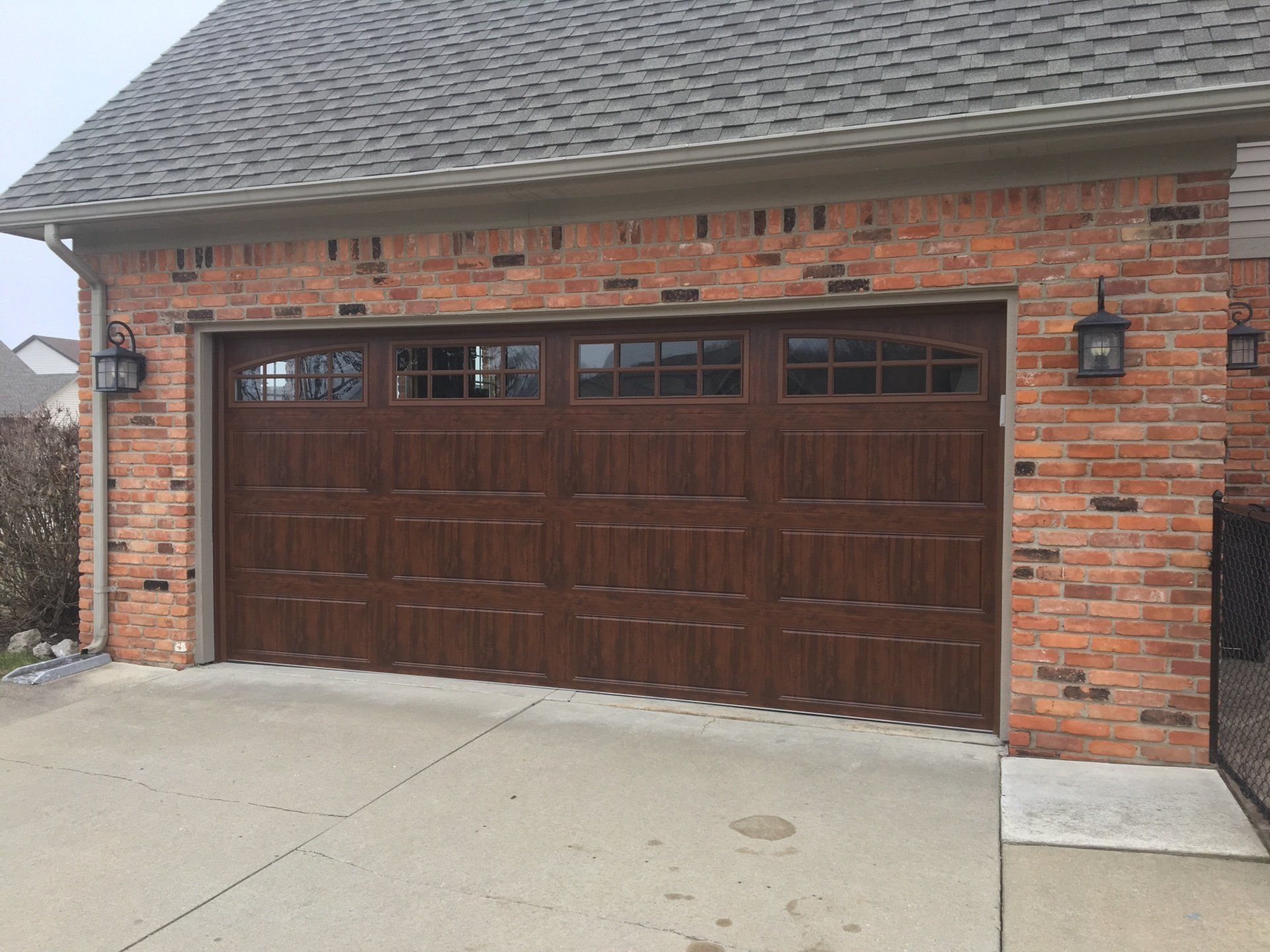 A brick garage with a brown garage door and a gray roof.