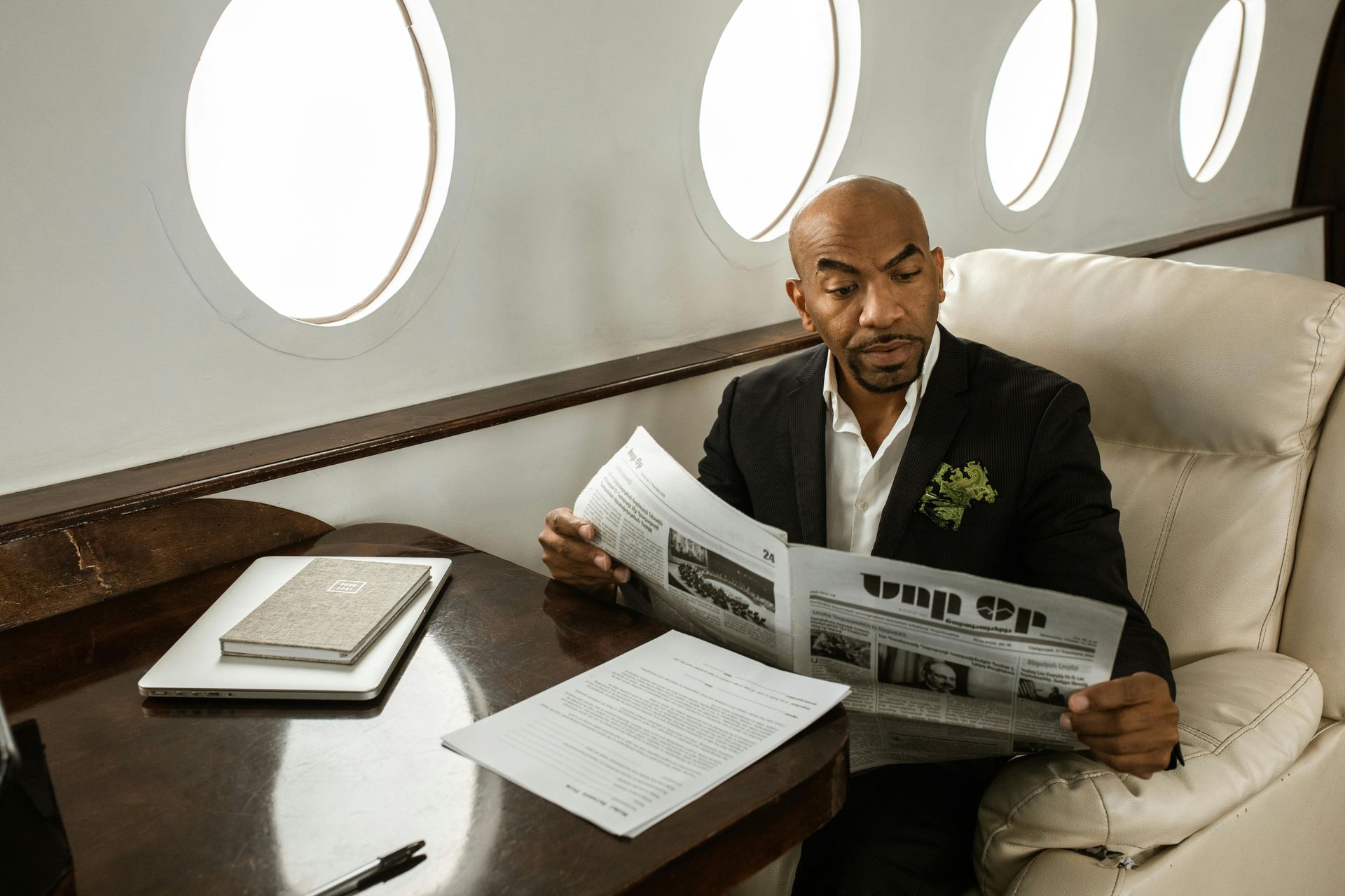 A man in a suit is reading a newspaper on a plane.