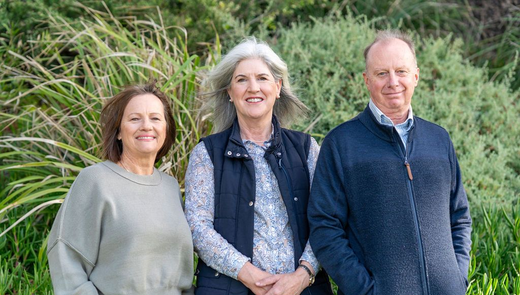 Three people standing outside: two women and a man, against green foliage — Dr John Salmon, Kiama Family Dental In Kiama, NSW