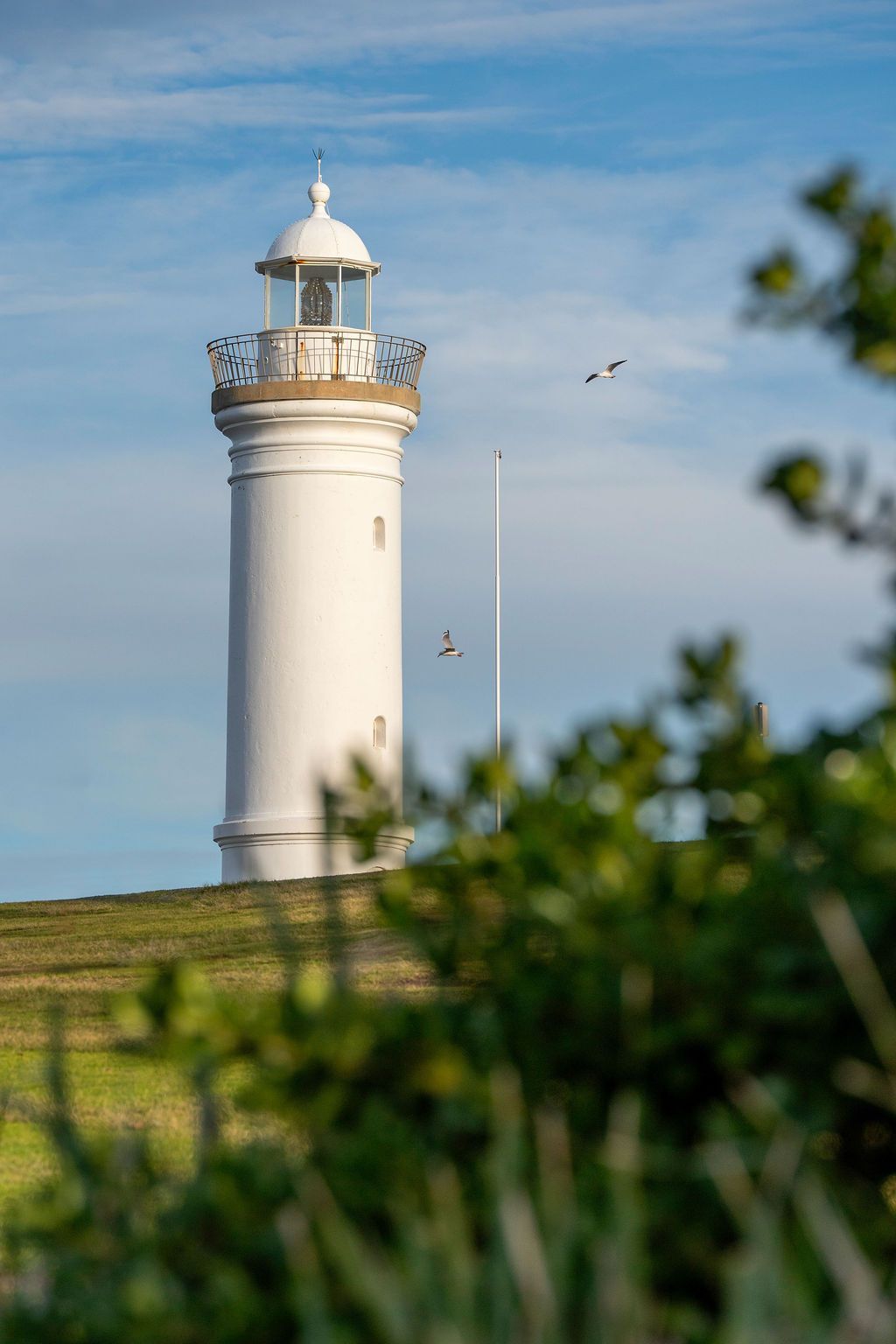 White Lighthouse on a Green Hill Under a Blue Sky — Dr John Salmon, Kiama Family Dental In Kiama, NSW