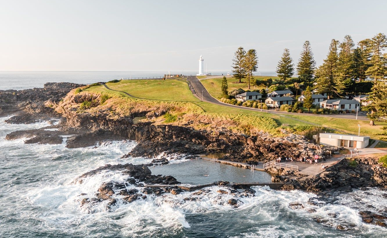 Ocean Waves Crashing Against Rocky Coastline, Grassy Cliff With Buildings — Dr John Salmon, Kiama Family Dental In Kiama, NSW