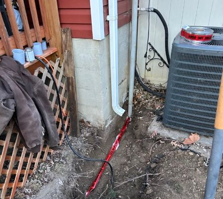 Broken underground cable, red insulation exposed, next to a downspout, air conditioner, and building.