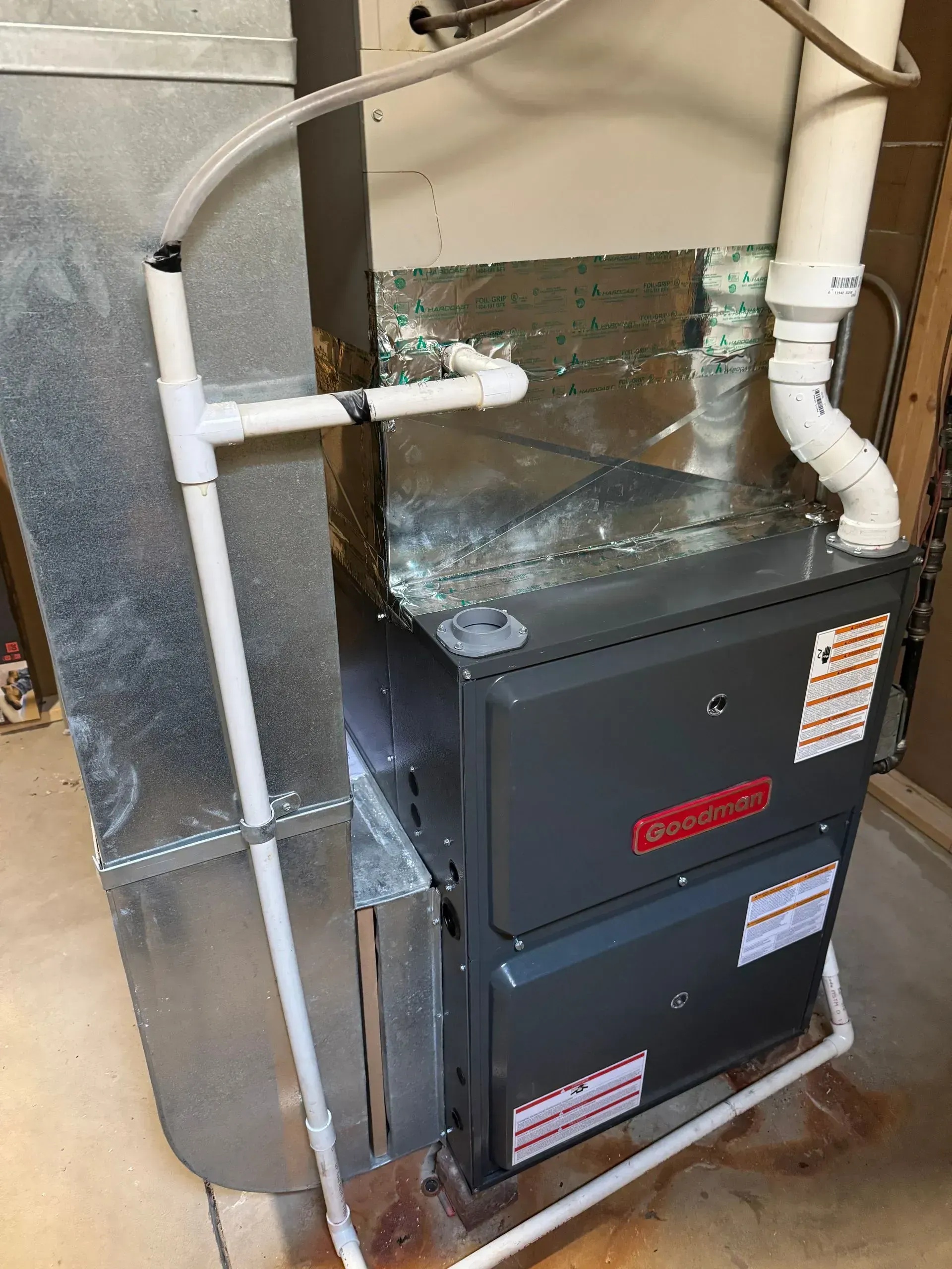 A furnace with attached ductwork and PVC piping in a utility room.