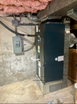 A dark HVAC unit and electrical box are in a basement next to concrete and pink insulation.