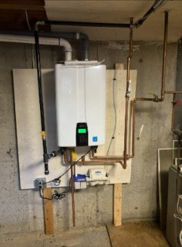 Tankless water heater mounted on a wall in a basement, with copper and black pipes.