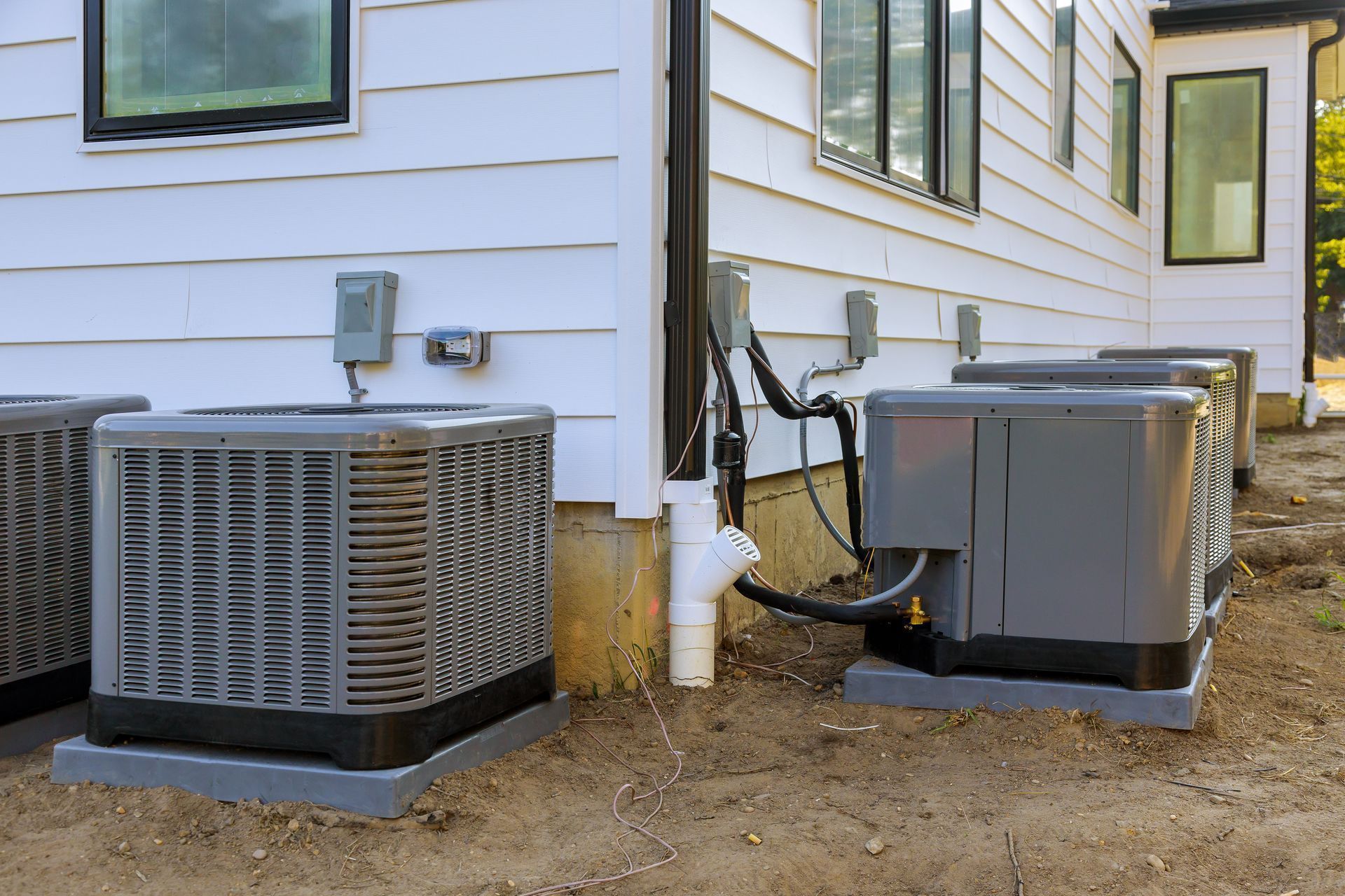 Several air conditioning units installed outside a white house with black-framed windows.