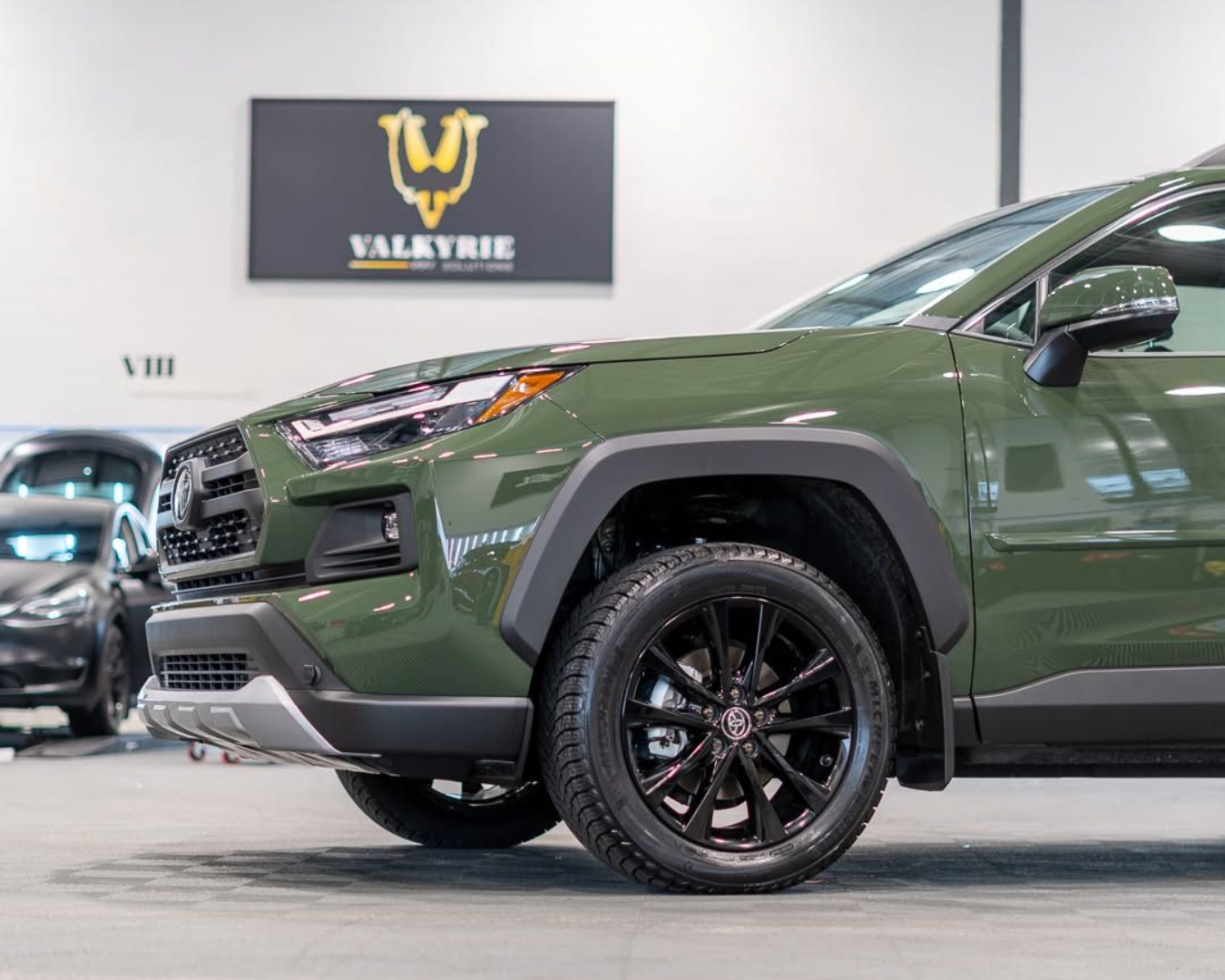 Green Toyota RAV4 SUV with black wheels in a showroom, under a 