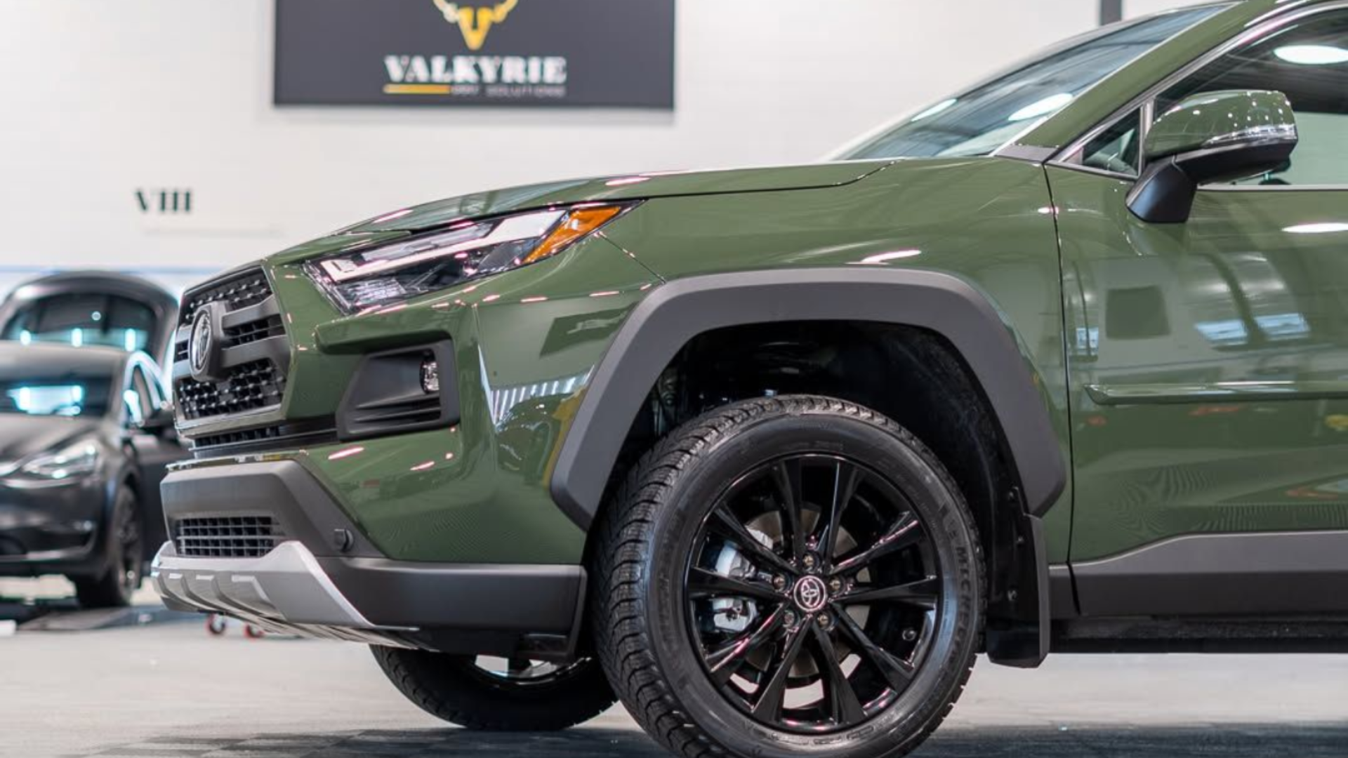Green Toyota RAV4 SUV with black wheels in a showroom, under a 