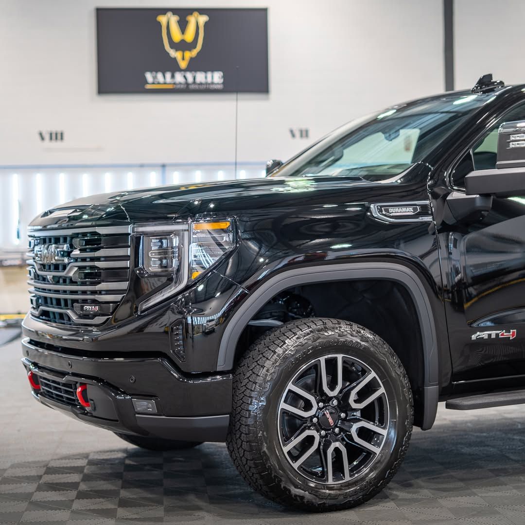 Black GMC AT4X truck with black and silver rims, parked indoors under a Valkyrie sign.