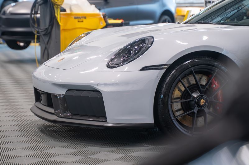 White Porsche sports car, close-up of front, showing black accents, gold-colored brake calipers. Indoor setting.