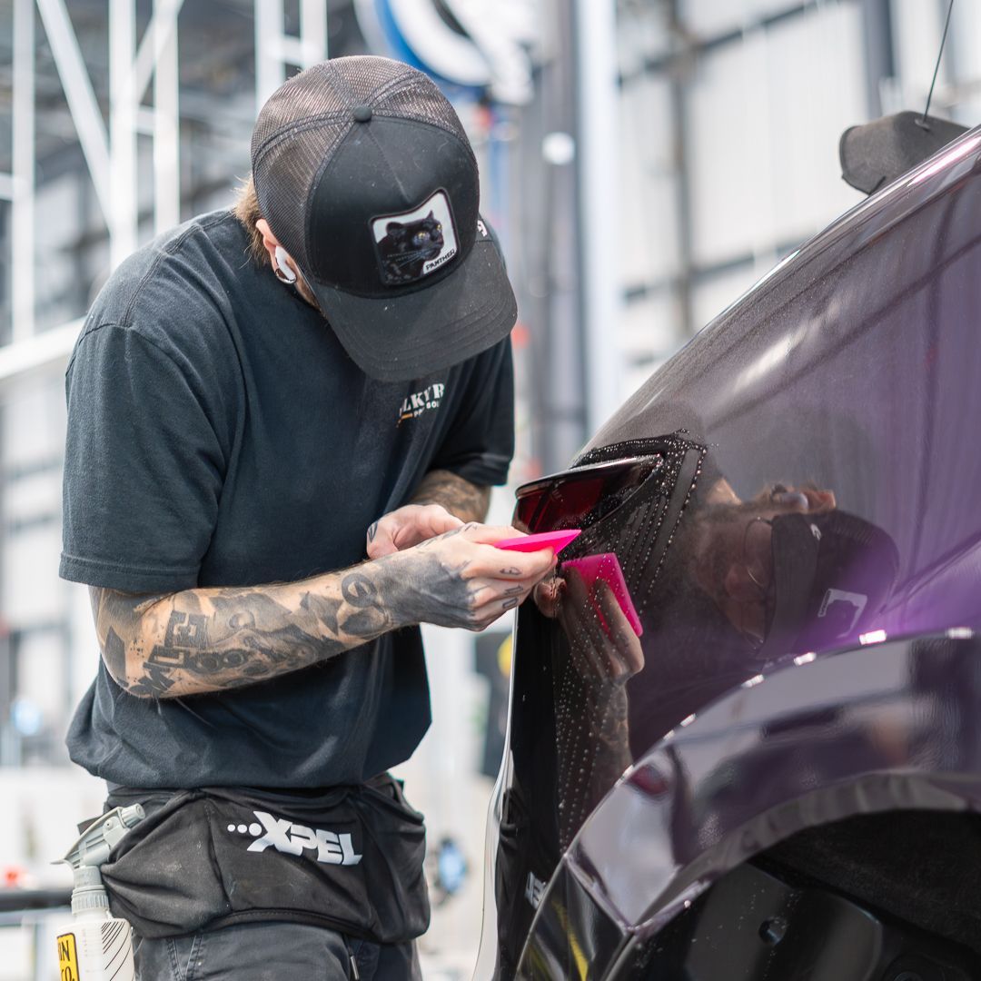 Person peeling protective film from a black car hood, likely applying paint protection film.