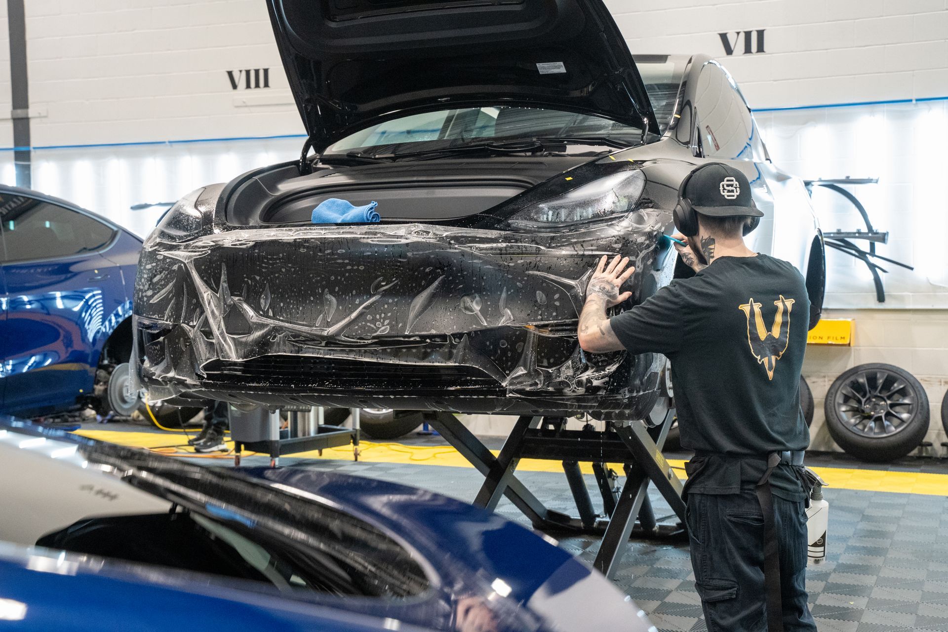 A man is working on a car in a garage with the hood open.