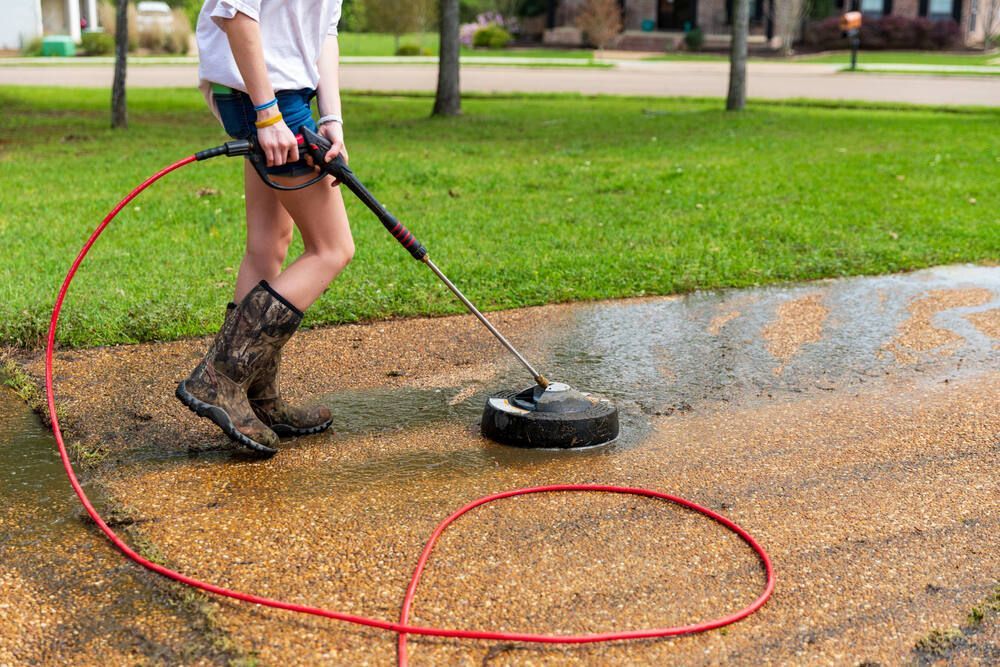 A Woman is Using a Pressure Washer to Clean a Driveway — Magic Wand Roof Restoration & Painting in Mermaid Beach, QLD