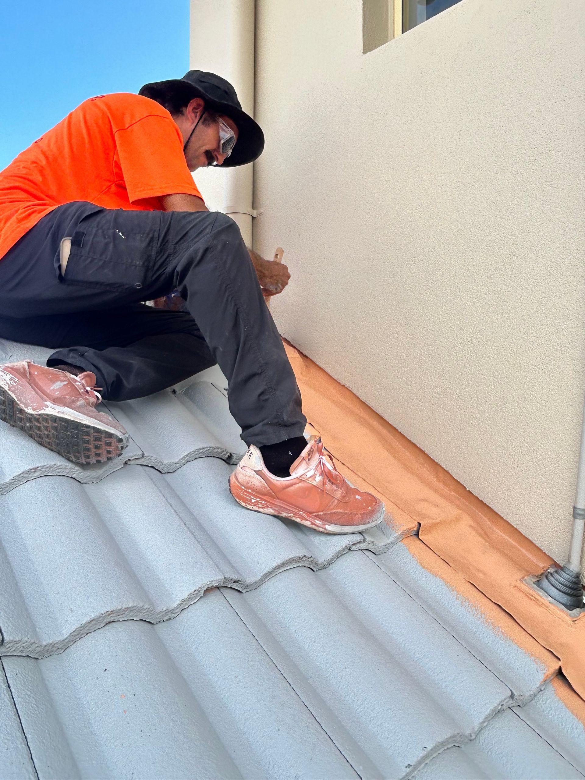 Person in orange shirt working on a roof, inspecting the wall of a building — Magic Wand Roof Restoration & Painting in Mermaid Beach, QLD