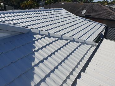 A Man is Painting the Roof of a House — Magic Wand Roof Restoration & Painting in Mermaid Beach, QLD