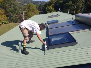 A Man is Painting the Roof of a Building With a Sprayer — Magic Wand Roof Restoration & Painting in Mermaid Beach, QLD