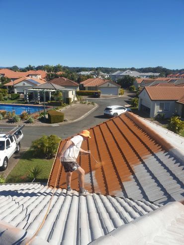 A Man is Painting on a Tiled Roof — Magic Wand Roof Restoration & Painting in Mermaid Beach, QLD