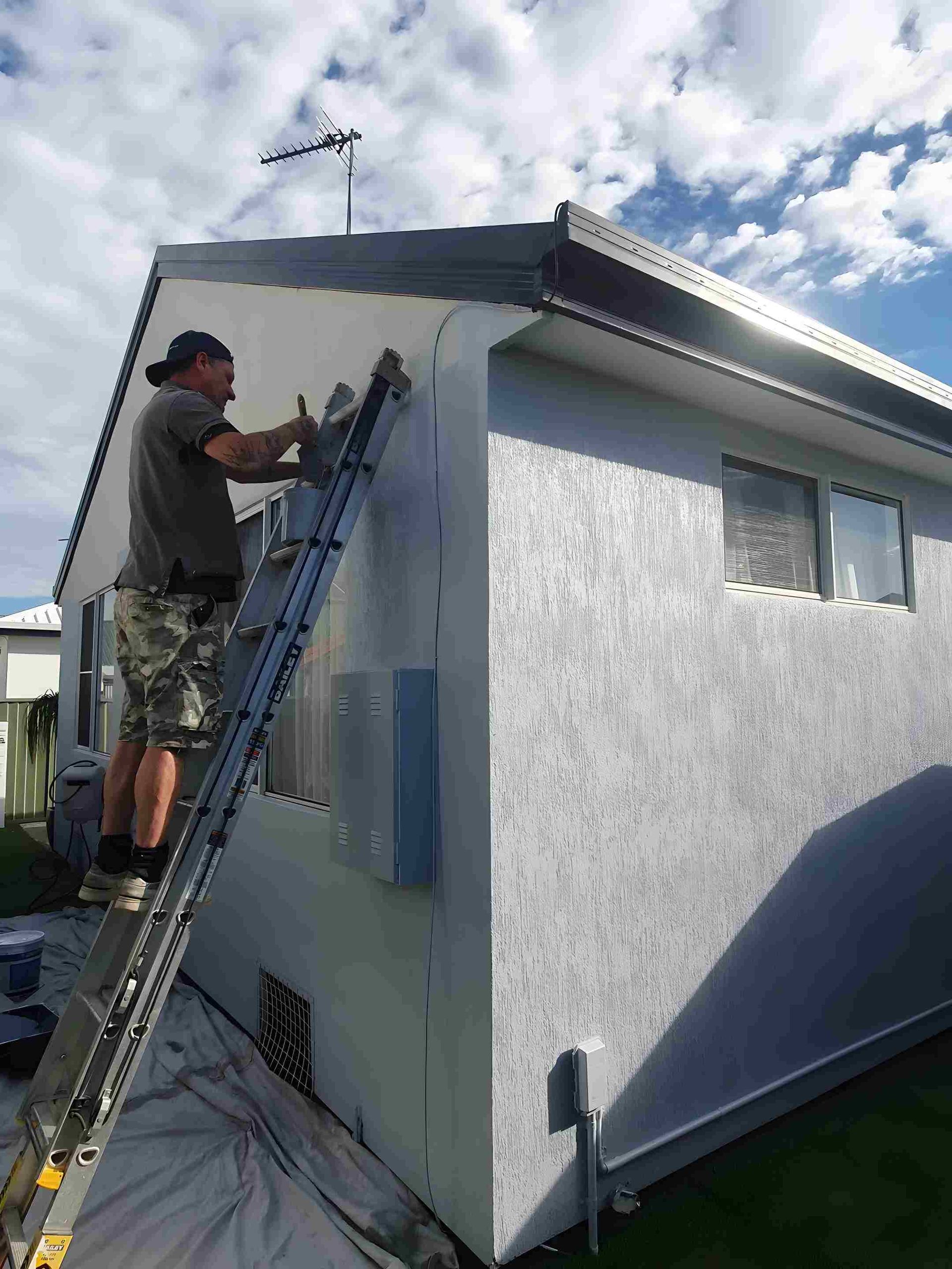 A man is painting the side of a house — Magic Wand Roof Restoration & Painting in Mermaid Beach, QLD