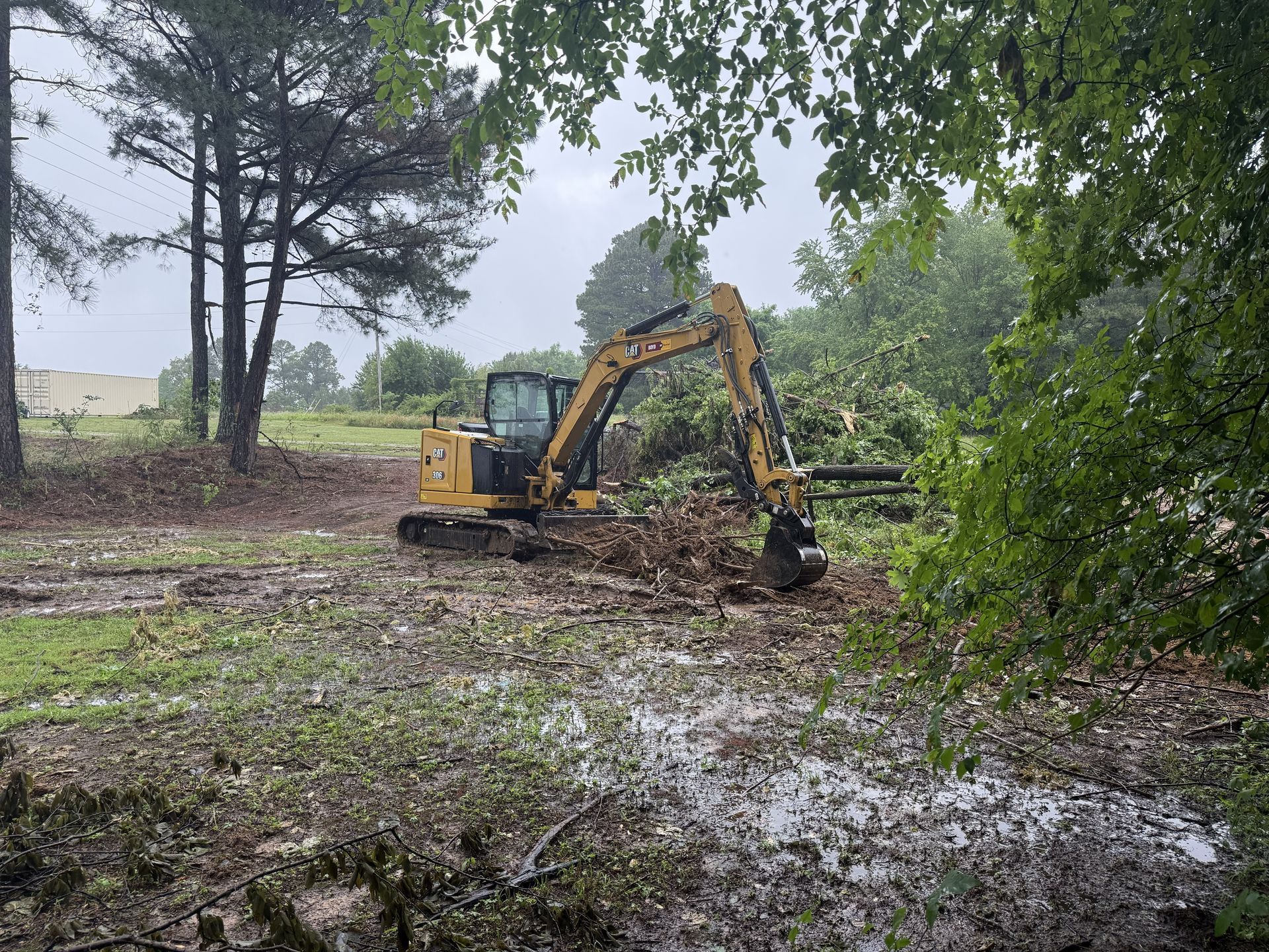 Yellow excavator clearing brush in a muddy wooded field