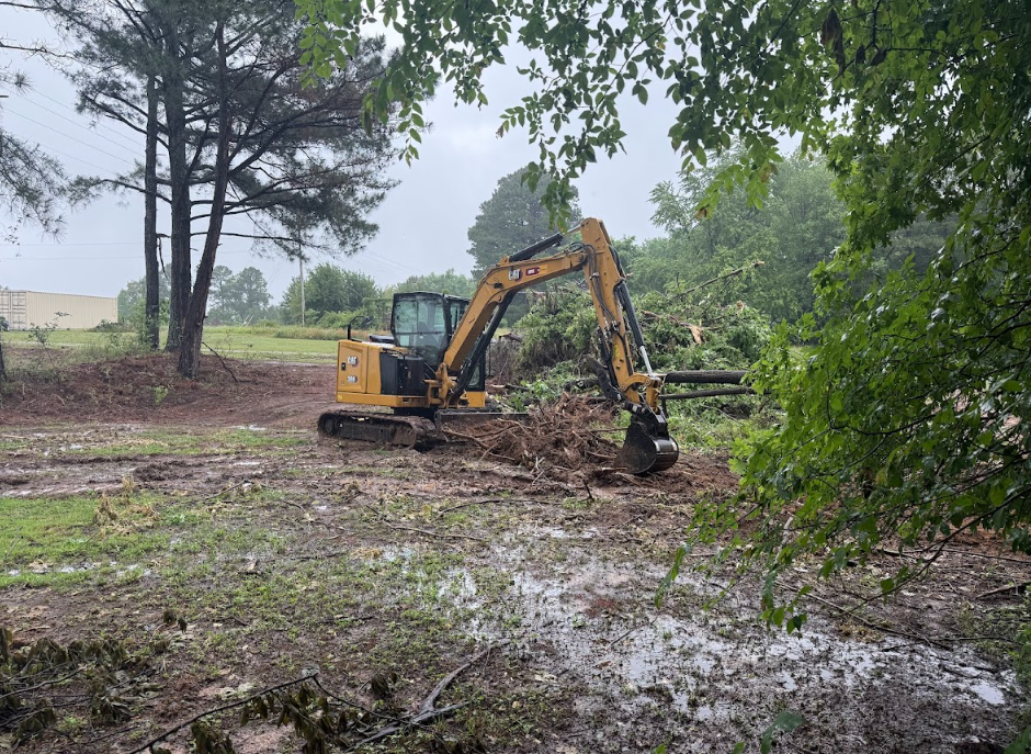 Yellow excavator clearing muddy ground in a wooded area