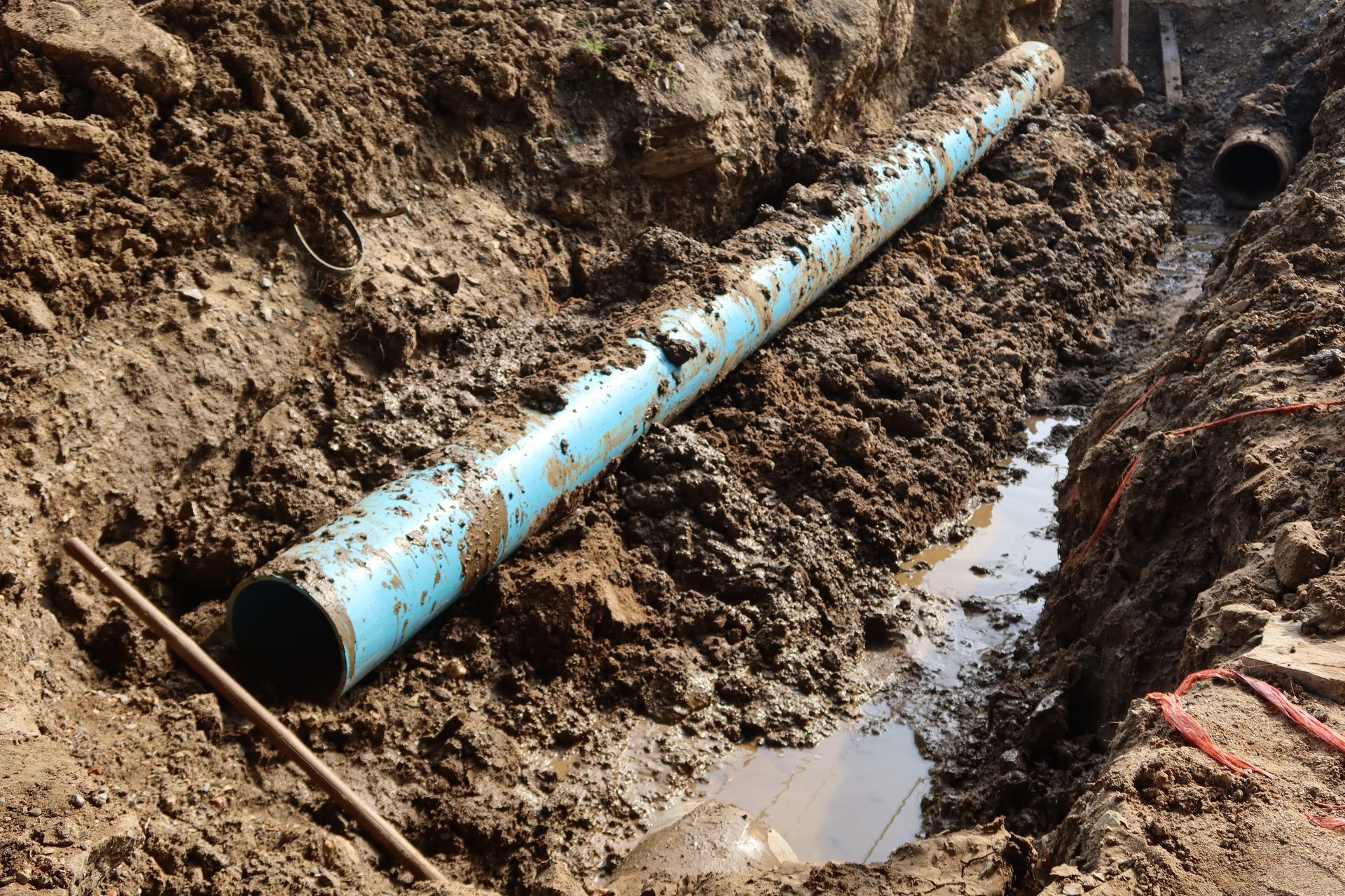 Blue pipe lying in a muddy trench with standing water during construction