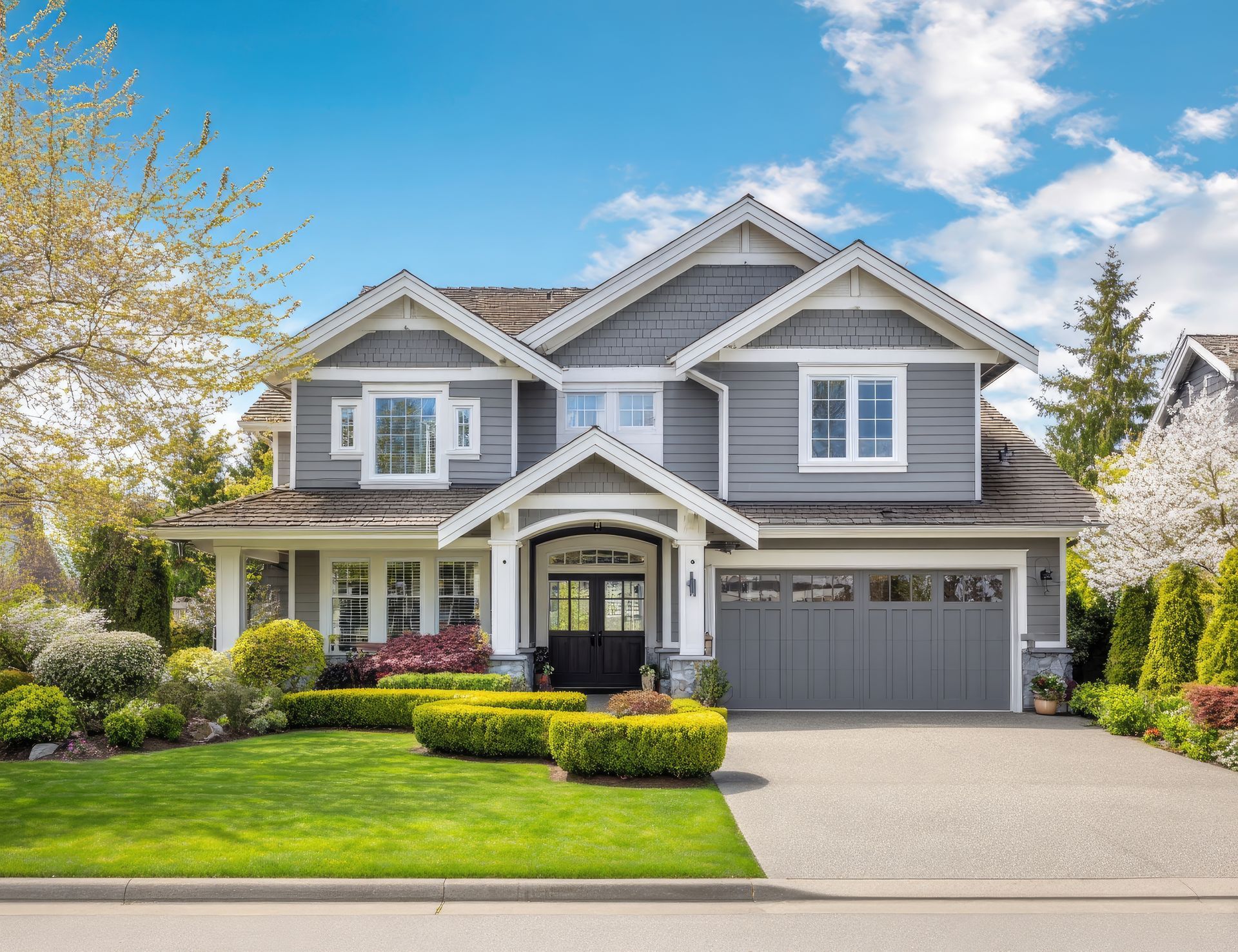 Gray two-story suburban house with white trim, manicured lawn, and attached garage under a blue sky