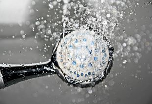 Showerhead spraying water, drops and droplets visible, close-up, metallic and gray tones.