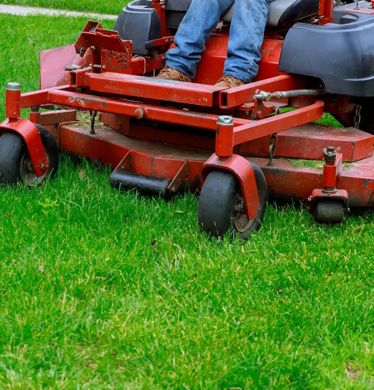 Person on a red zero-turn mower cutting green grass.