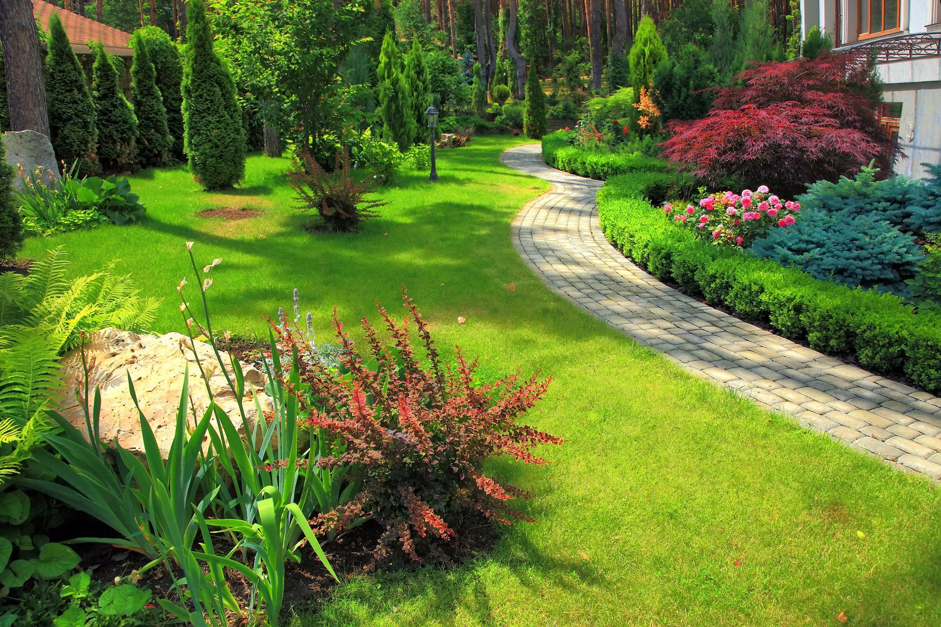 Manicured garden with a stone pathway, vibrant green grass, and colorful shrubs.