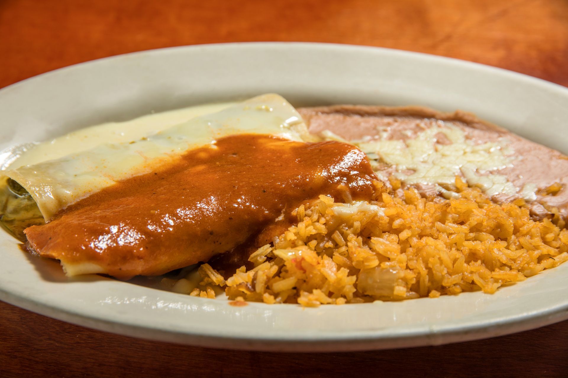 A plate of mexican food with rice and enchiladas on a table.