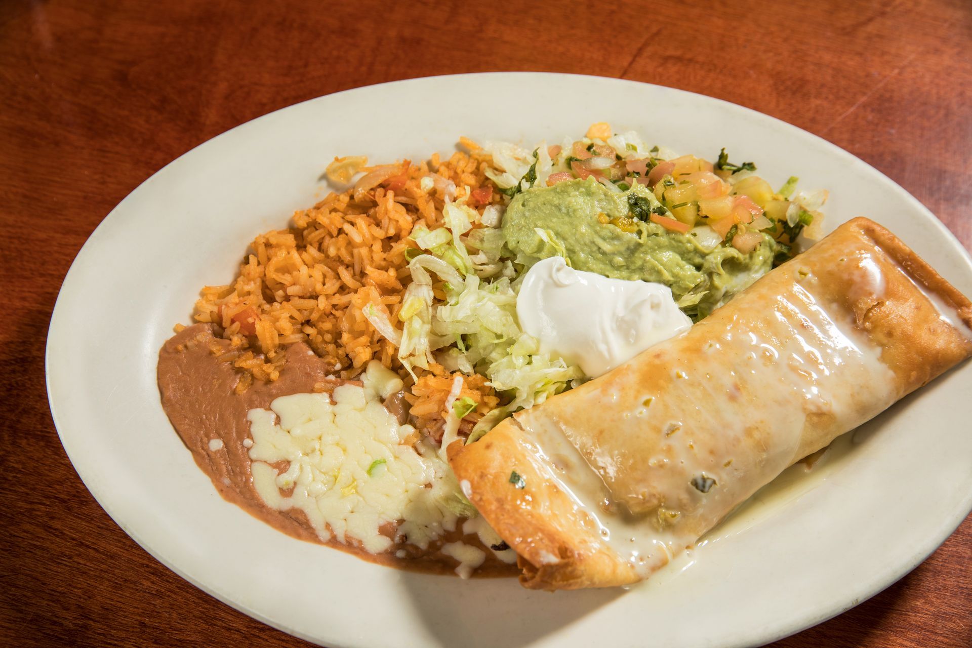 A white plate topped with a burrito , rice , beans and guacamole.