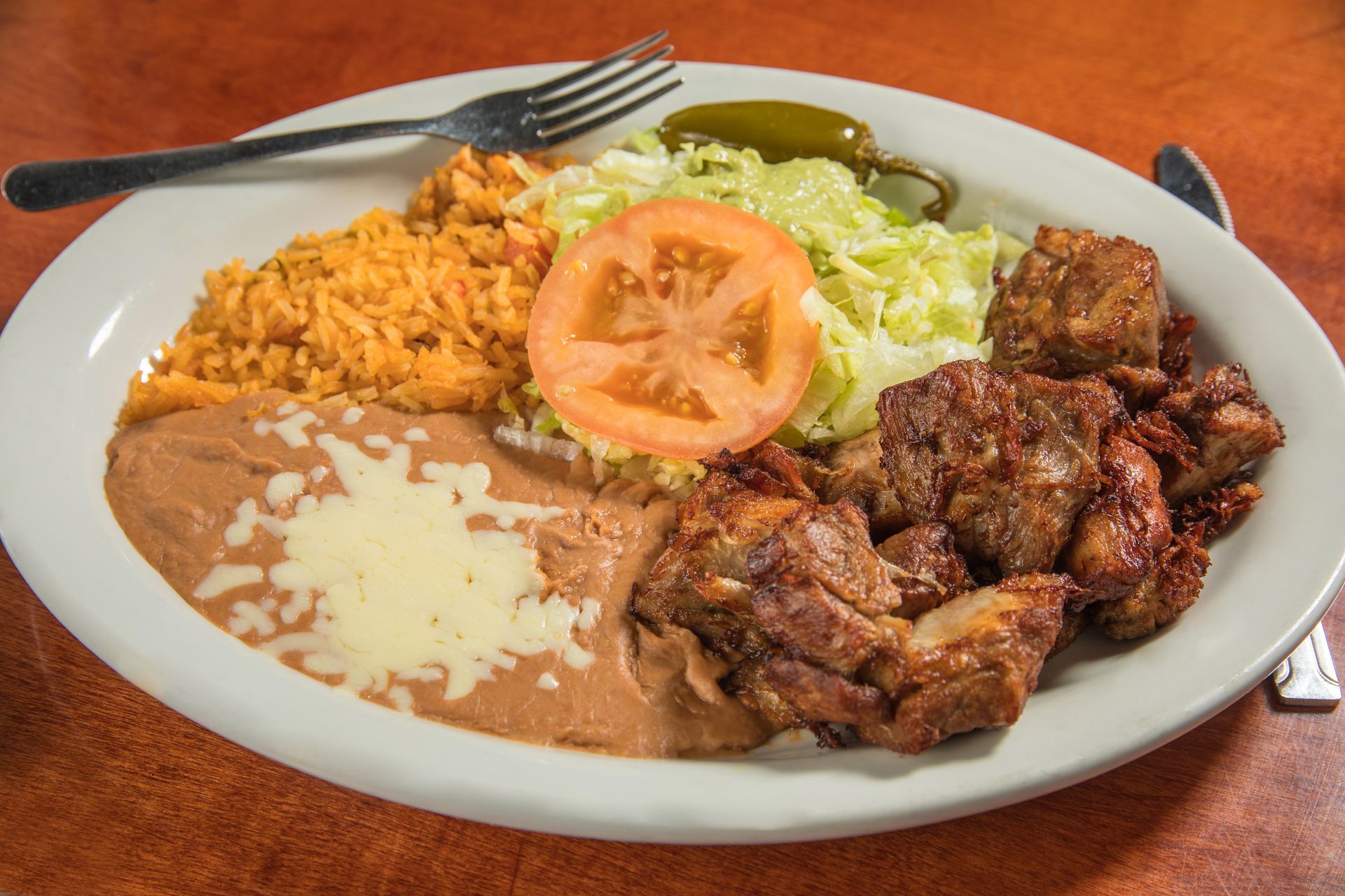 A white plate topped with meat , beans , rice and lettuce with a fork.