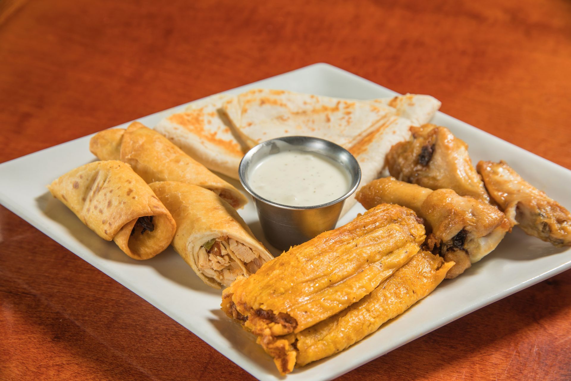 A white plate topped with a variety of food , including chicken wings and quesadillas.