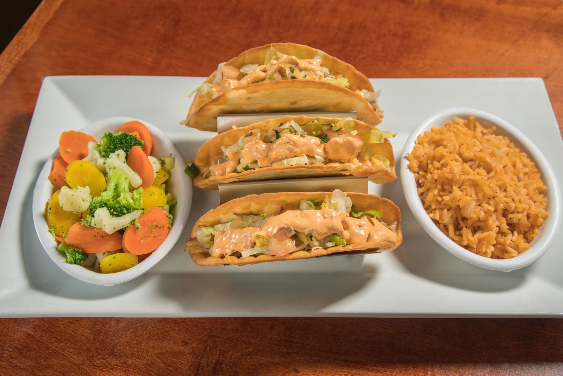 A white plate topped with tacos , rice and vegetables.