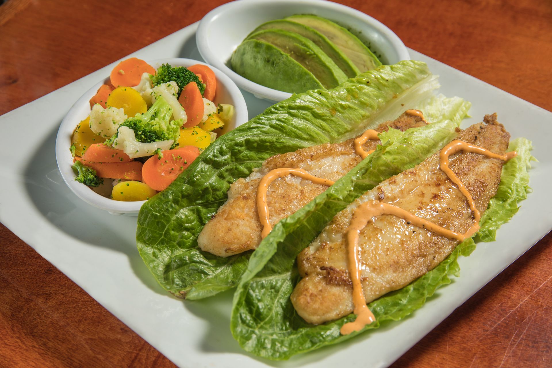 A white plate topped with fish , lettuce , avocado and vegetables.