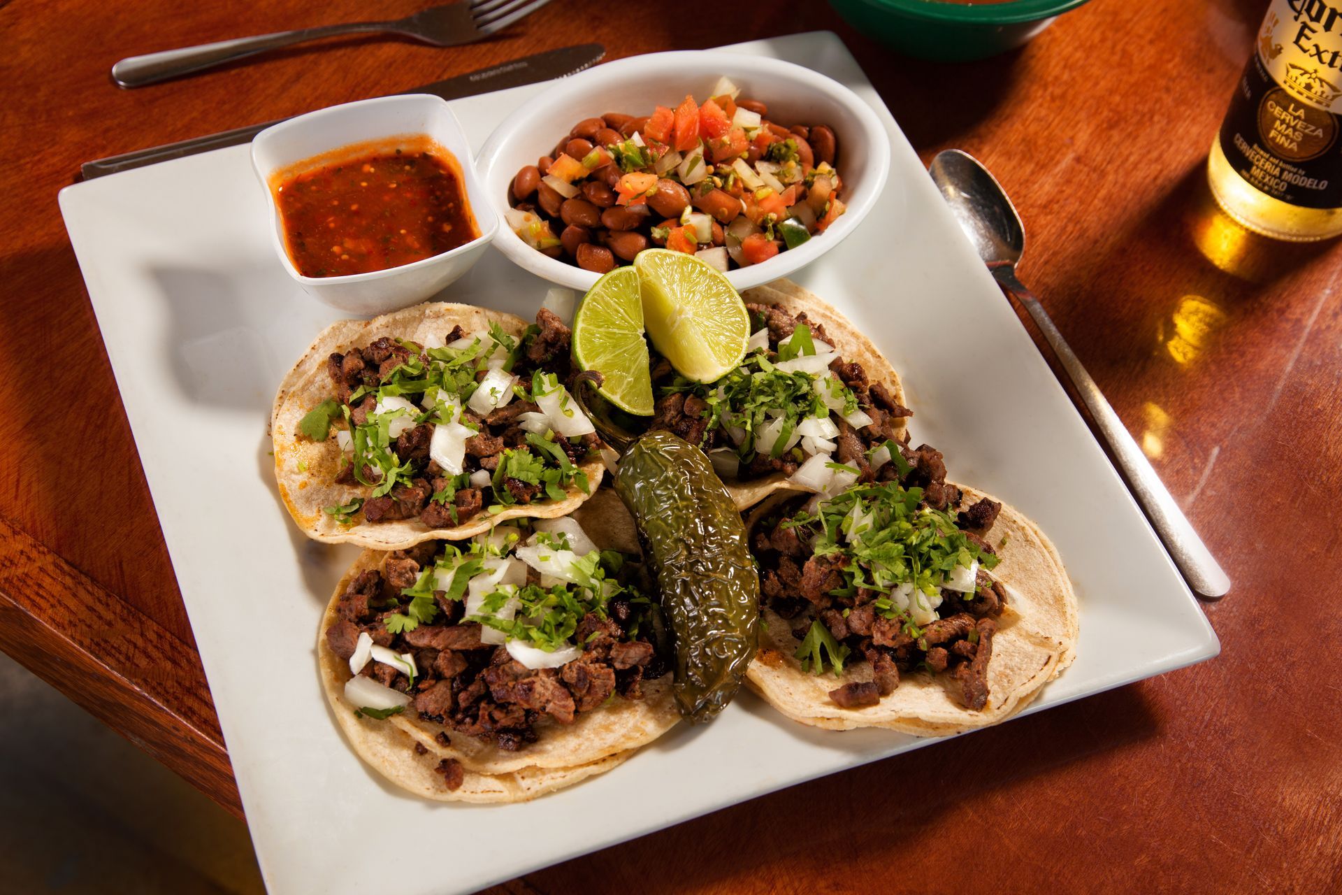 A white plate topped with tacos and a bottle of corona beer