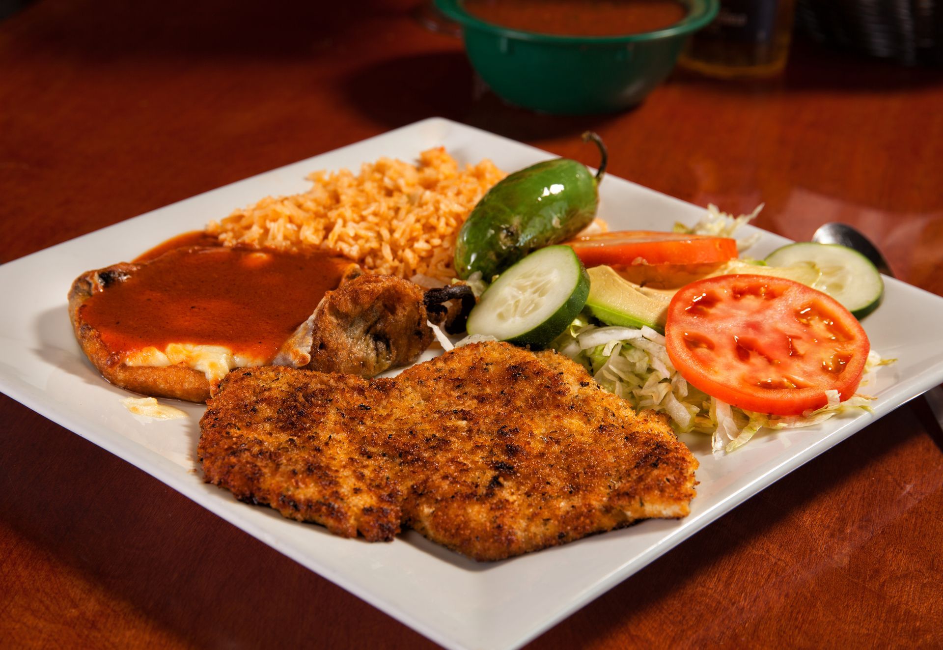 A white plate topped with chicken , rice and vegetables on a table.