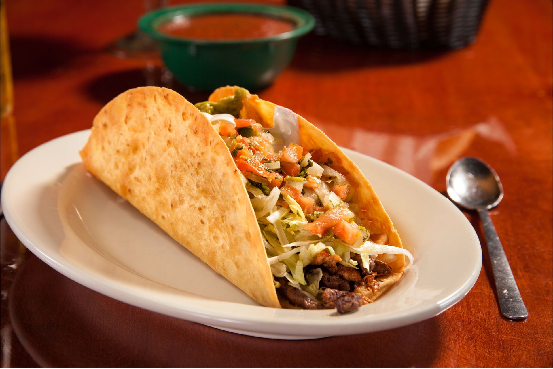 A taco on a white plate next to a spoon