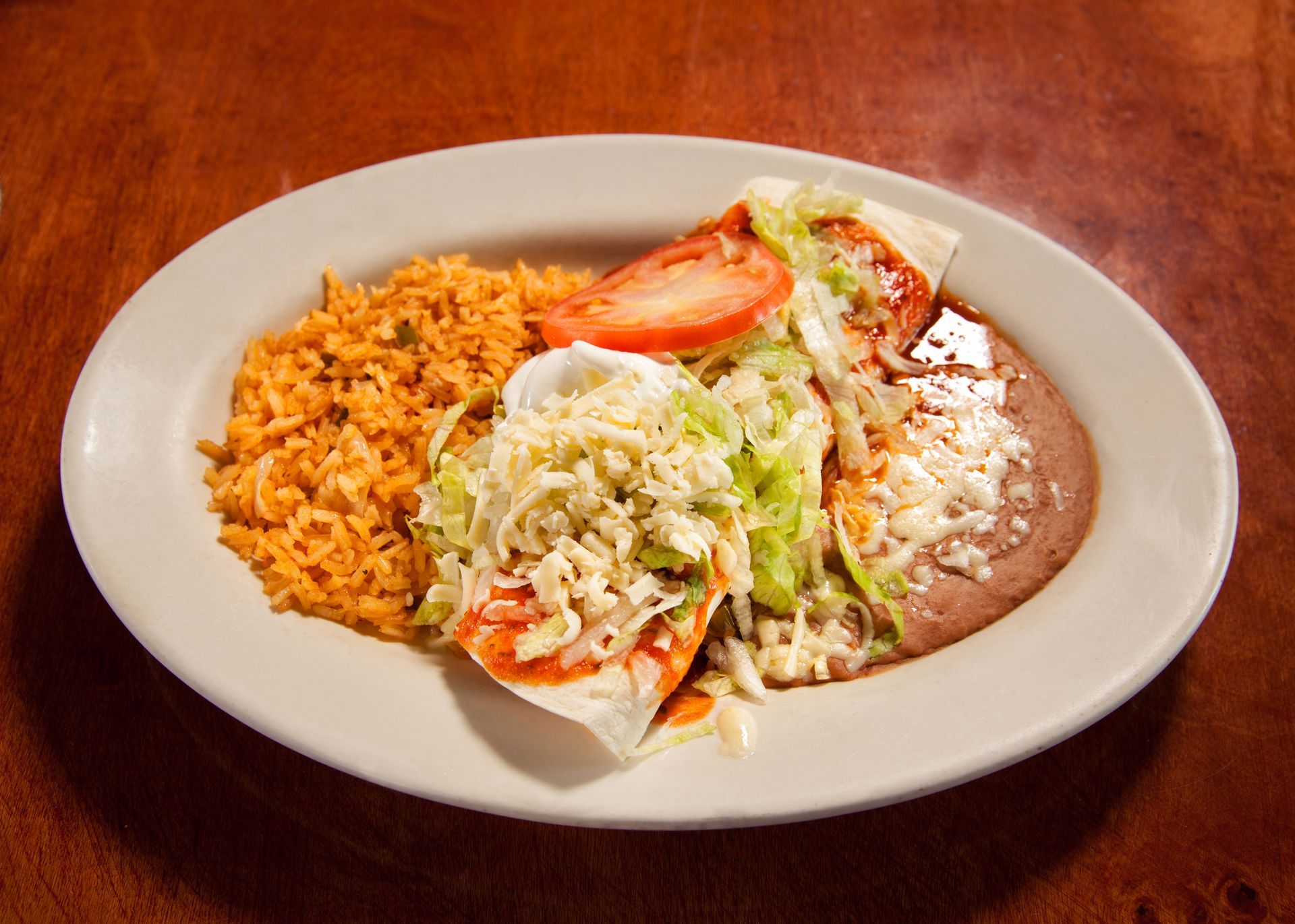 A plate of mexican food with rice and beans on a wooden table.