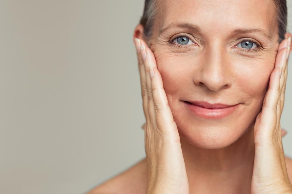 A Woman Is Touching Her Face With Her Hands And Smiling — Mackay Skin Clinic In North Mackay, QLD