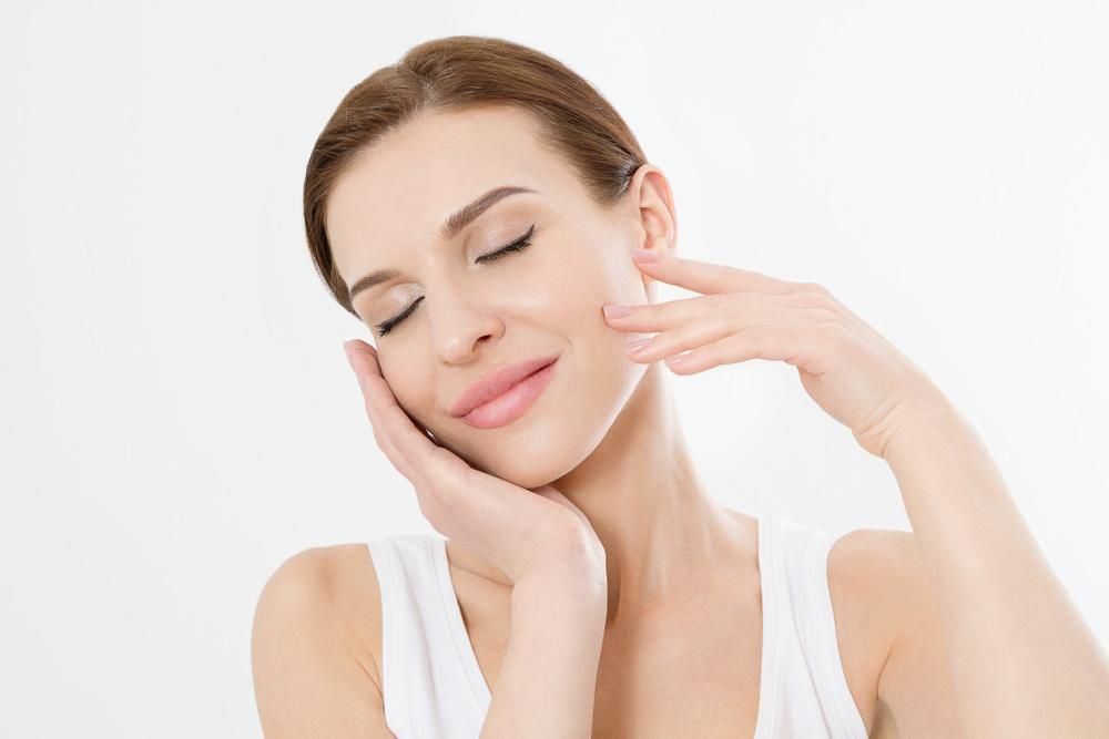 A Woman Is Touching Her Face With Her Hands And Smiling — Mackay Skin Clinic In North Mackay, QLD